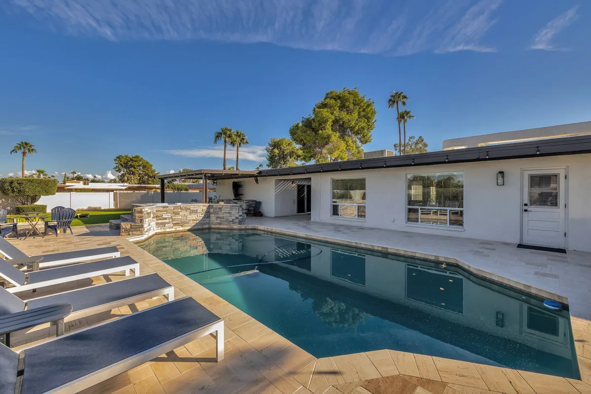 A sparkling swimming pool flanked by stylish outdoor loungers, a landscaped garden, and a spacious patio area. The scene feels cheerful and relaxed, ideal for swimming, sunbathing, or gathering with friends for outdoor dining.