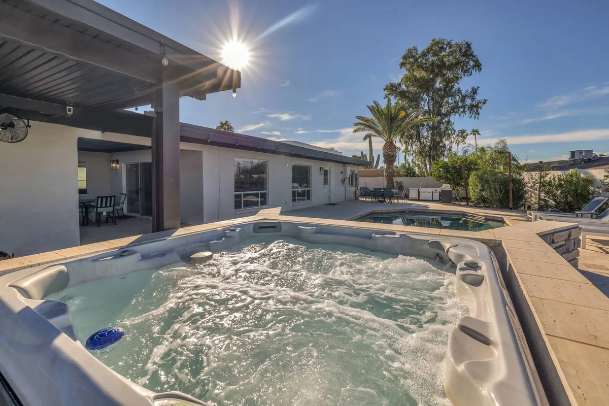 A backyard oasis featuring a sparkling swimming pool, bubbling hot tub, swaying palm trees, and sun-drenched seating areas. The scene is inviting and tranquil, perfect for relaxation and downtime between appointments.