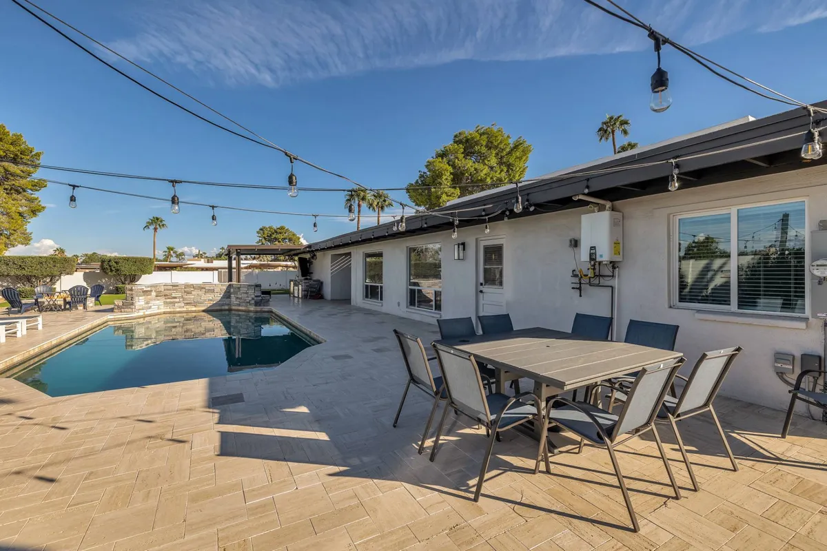 An inviting outdoor scene with a shimmering swimming pool, dining table set under string lights, and a landscaped garden. The setup is ideal for sunset dinners, morning coffees, and evening celebrations, emphasizing the joy of spending time together outdoors.