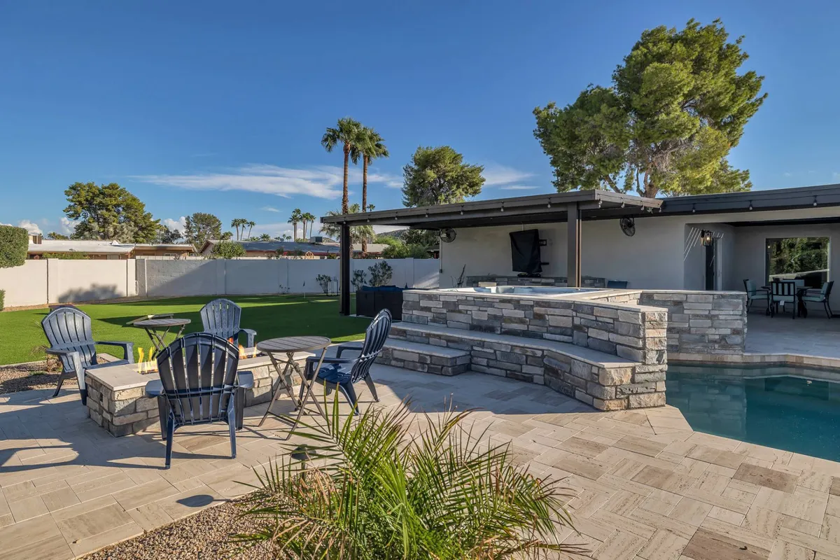 A sun-drenched backyard featuring a sparkling private pool bordered by lush landscaping and ample patio seating, inviting guests to swim, sunbathe, and socialize. The BBQ area is set up for outdoor cooking and gatherings, perfect for group celebrations and relaxation.