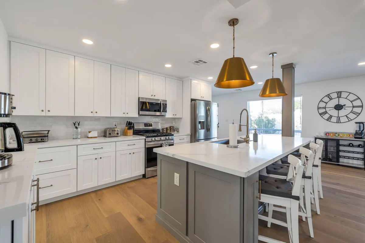 Showcasing a modern kitchen, this image focuses on the large island with seating, gleaming stainless steel appliances, gold pendant lights, and fresh white cabinetry. The overall design is functional yet stylish, perfect for meal preparation, entertaining, or simply sharing snacks.