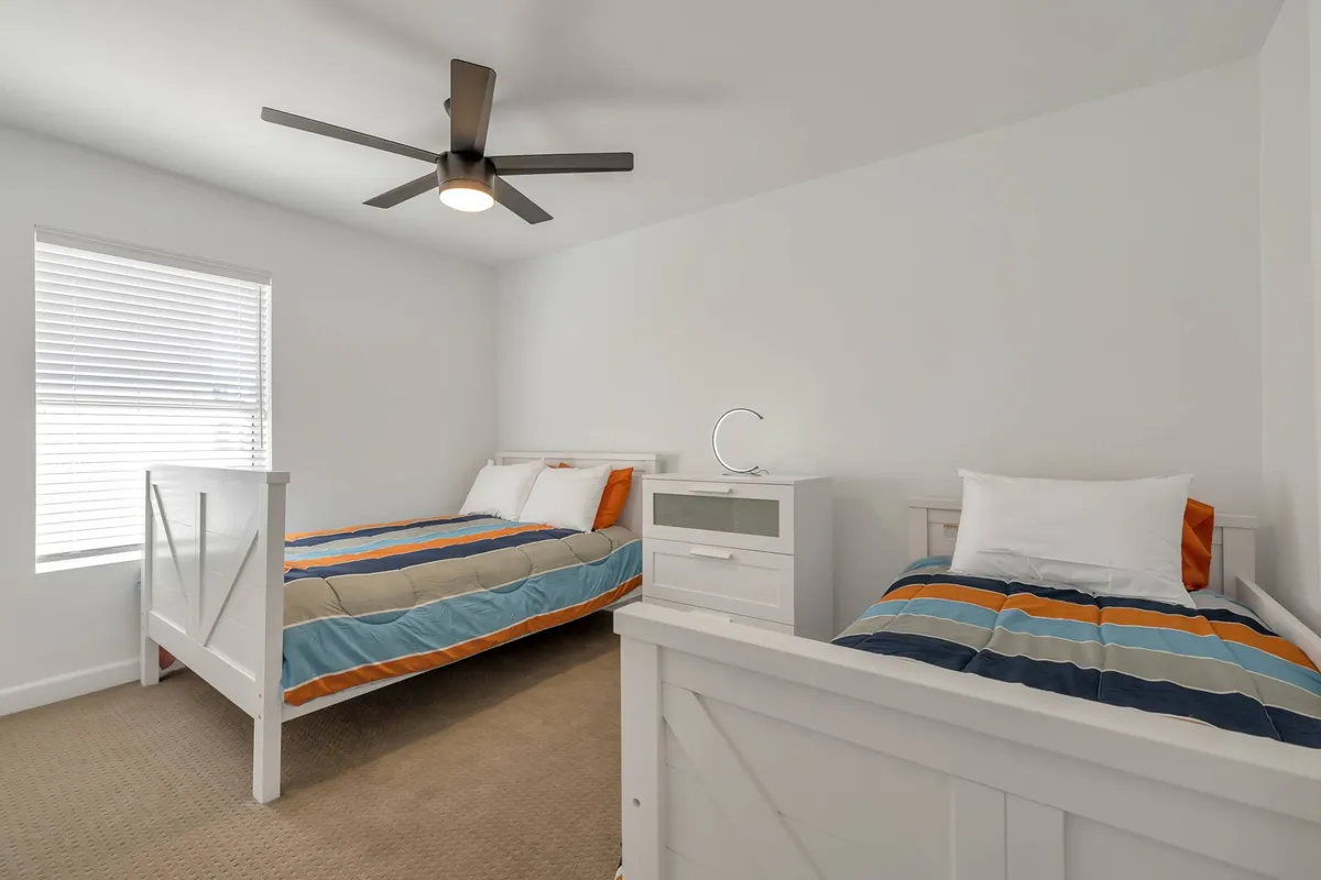 A family-friendly bedroom displaying two beds—a full and a twin—each with comfortable bedding. The room is brightened by natural light from a window, and includes a ceiling fan and practical nightstand, creating a versatile and inviting atmosphere.