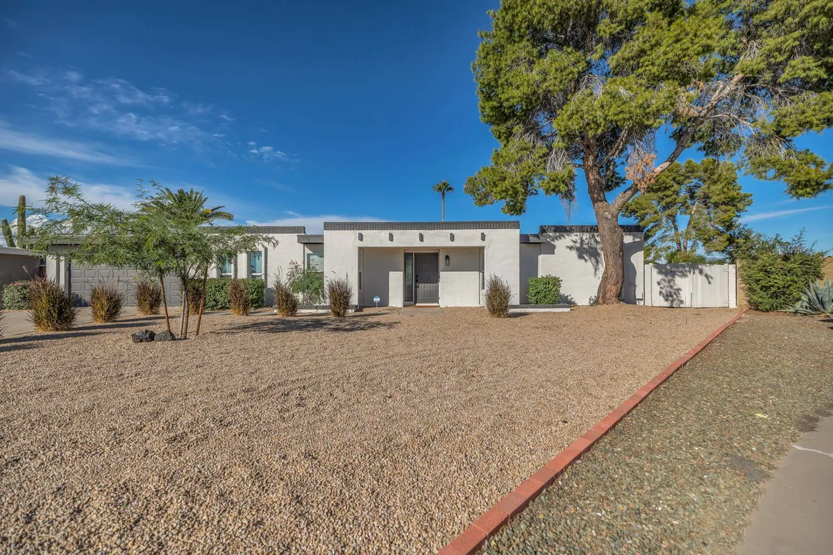 A welcoming exterior view showcasing modern architecture, a landscaped gravel yard, a large mature tree, and the inviting front entrance. The scene conveys an immediate sense of arrival in a tranquil residential setting, ideal for guests seeking comfort near Mayo Clinic.