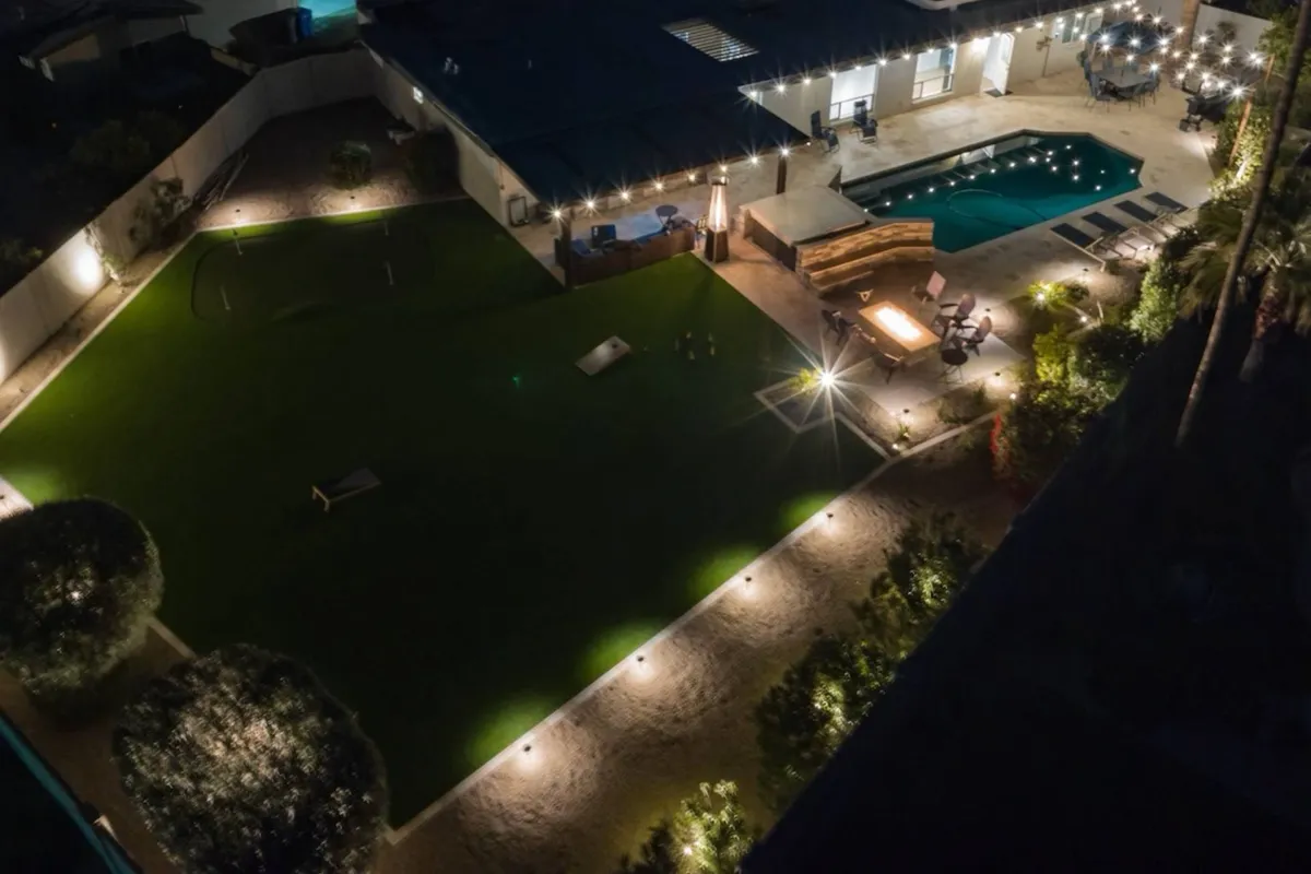 This image showcases a beautiful backyard scene featuring a sparkling swimming pool, a cozy fire pit area, and ample outdoor seating. The carefully landscaped lawn and lighting create a warm and inviting space, perfect for evening gatherings or relaxing by the water.