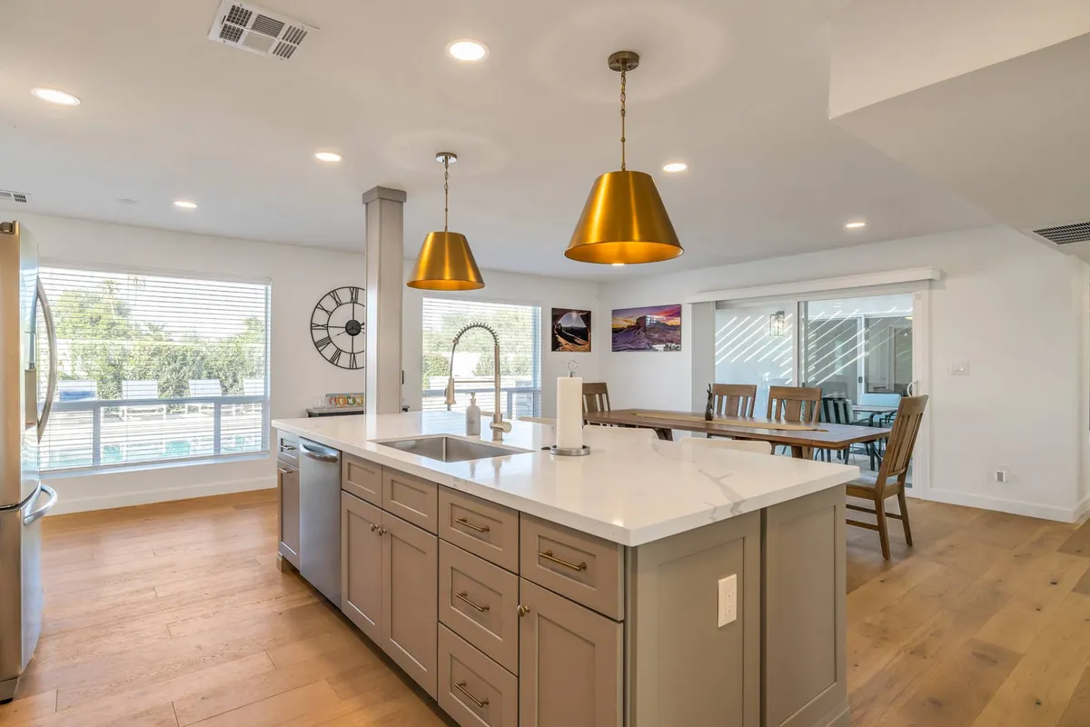 A bright, open-plan kitchen and dining area with a large island, elegant gold pendant lights, and a welcoming dining table. The arrangement encourages cooking, shared meals, and communal celebrations, fostering a social and inclusive atmosphere.