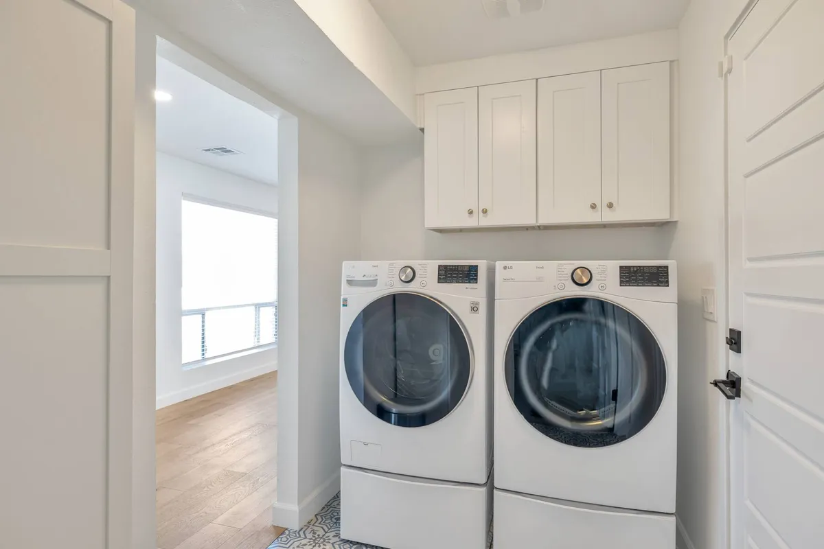 A dedicated laundry area featuring a modern washer and dryer set, white cabinetry above for storage, and sleek flooring, creating a bright and organized space ideal for handling daily chores.