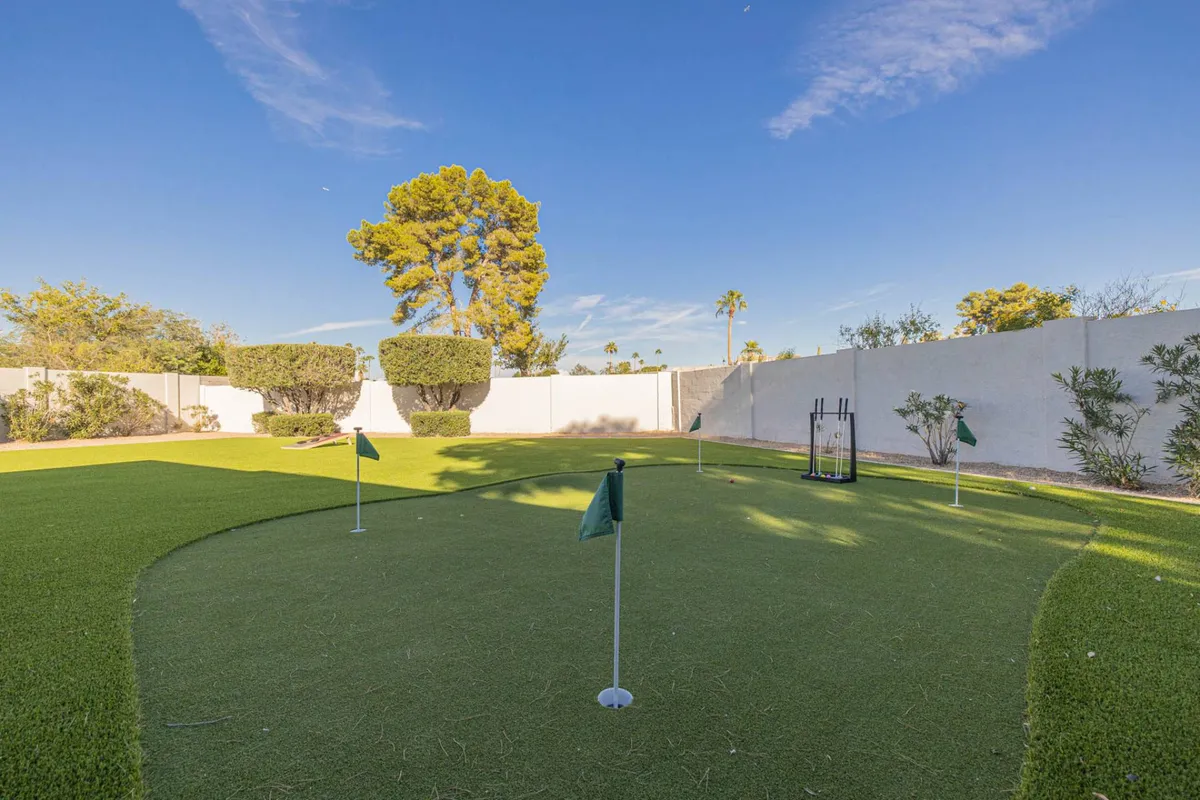 This image features a well-maintained putting green surrounded by trees and landscape features. The space is open and bright, ideal for practicing golf or enjoying a leisurely afternoon outdoors.
