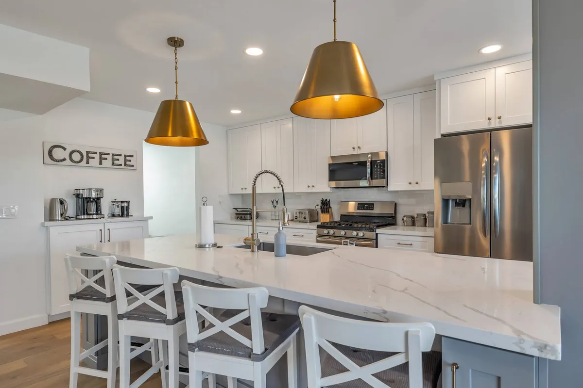 A bright and inviting kitchen corner showcasing a marble countertop, gold pendant lights, and a well-appointed coffee station, suggesting adjacent access and modern convenience.