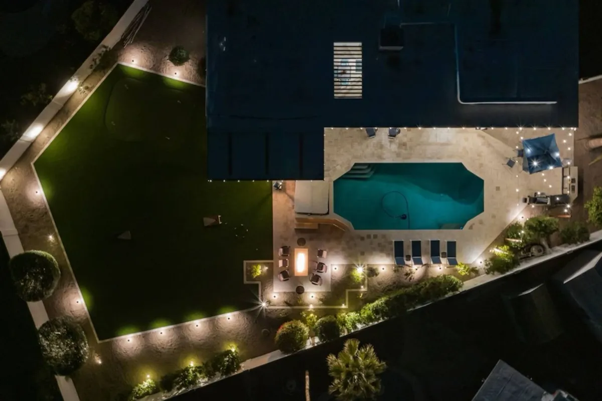 This exterior image features a sparkling swimming pool surrounded by a comfortable outdoor seating area, lush green lawn, and landscaped lighting. The space is set up for evening enjoyment, suggesting opportunities for stargazing, relaxing by the pool, or hosting social gatherings under the stars.